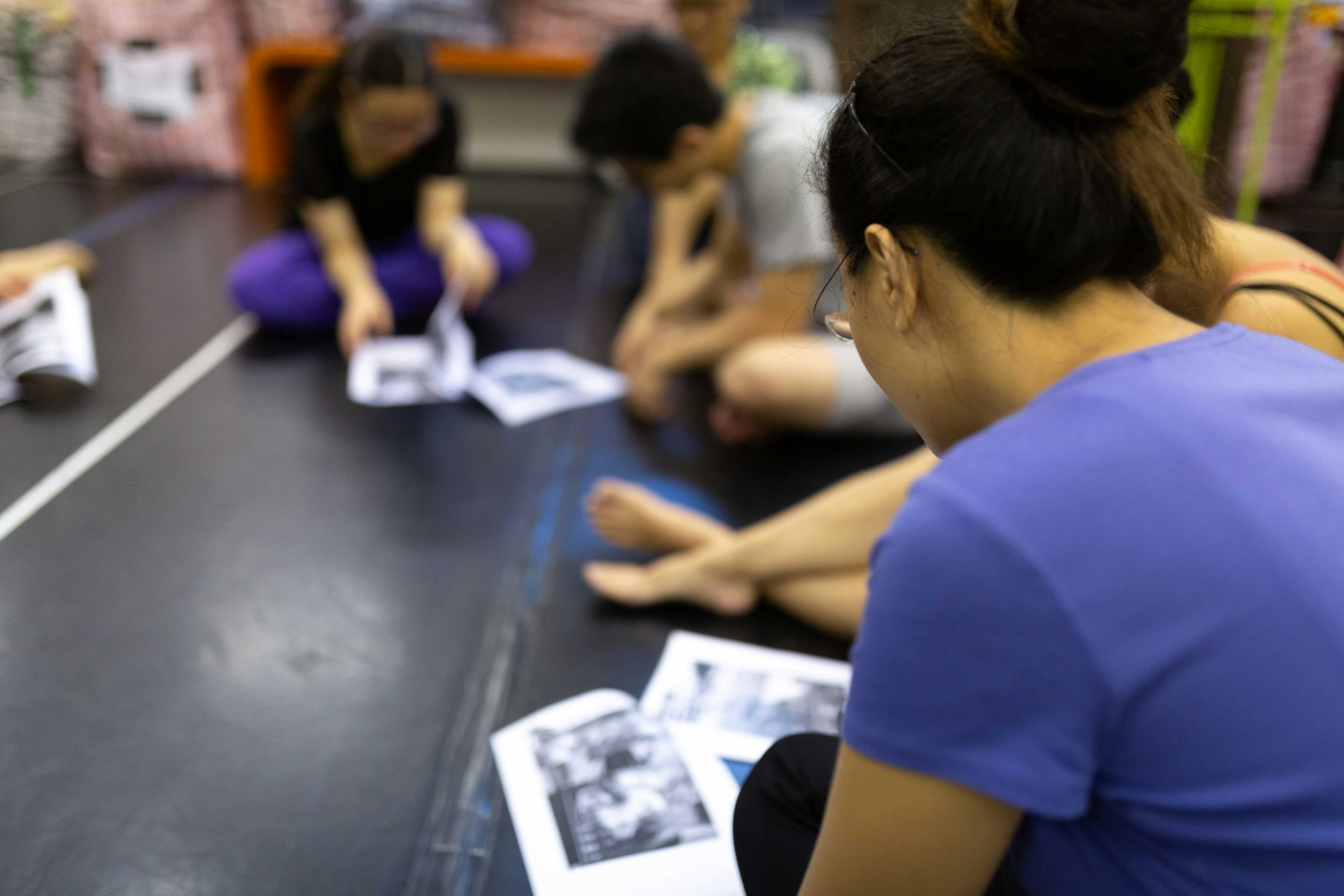Rooftop Productions • Hong Kong School Drama Courses | Michelle sitting on the floor going over a document with participants in a drama course | Rooftop Productions • Hong Kong Theatre Company